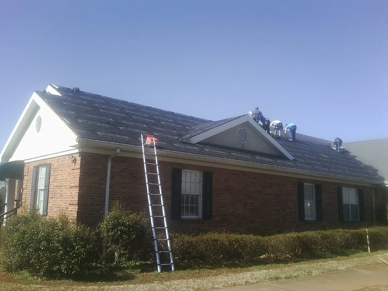Crew tearing shingles off a brick ranch roof with a ladder set — Metal Roof Repair work by our crew in Slippery Rock