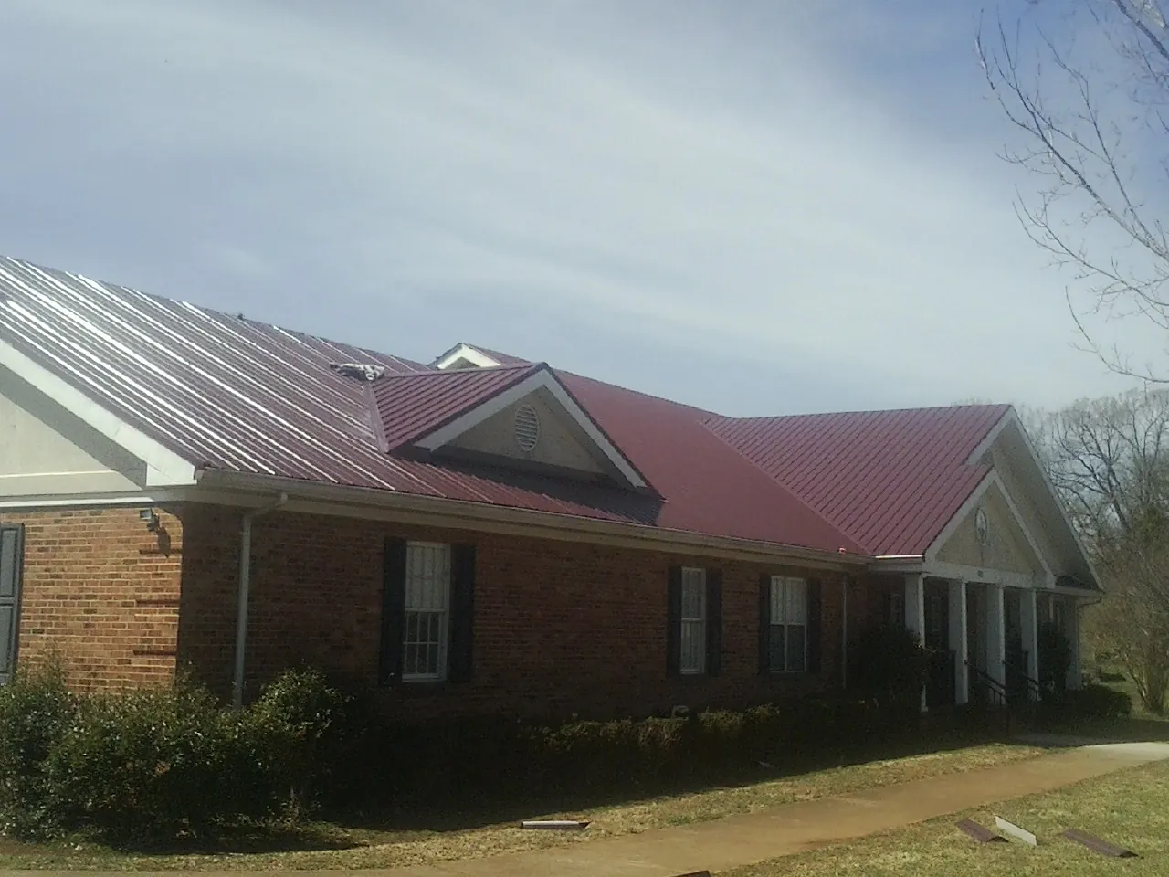 Red metal roof with gabled entries on a long brick building, from a Hail Damage Roof Repair job in Slippery Rock