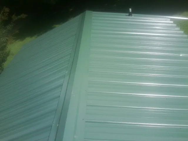 New green metal panels meeting at the ridge of a roof — Flat Roof Repair work by our crew in Slippery Rock