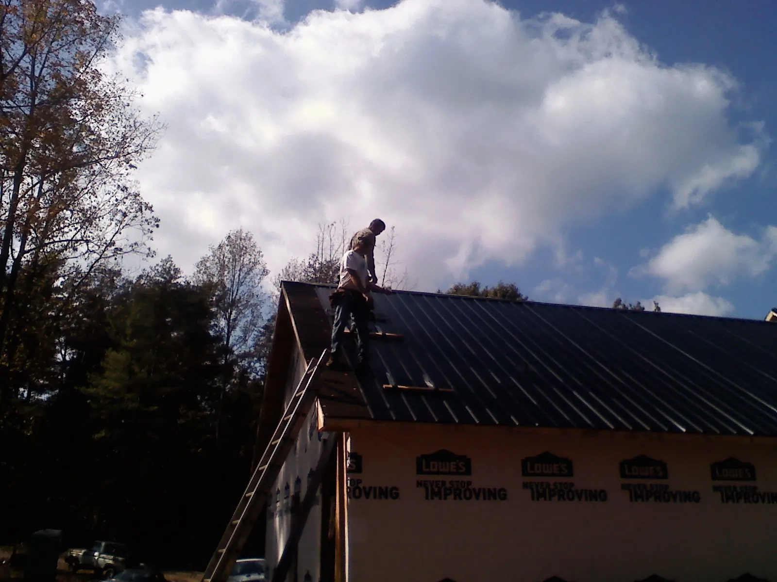 Roofer fastening dark metal panels high against a cloudy sky, from a Roof Inspection job in Slippery Rock