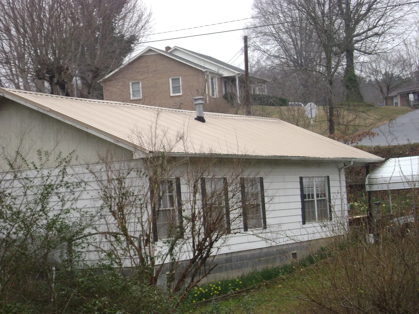 Tan metal roof on a white sided house set into a hillside — Commercial Roofing by Roofing Brothers in Slippery Rock