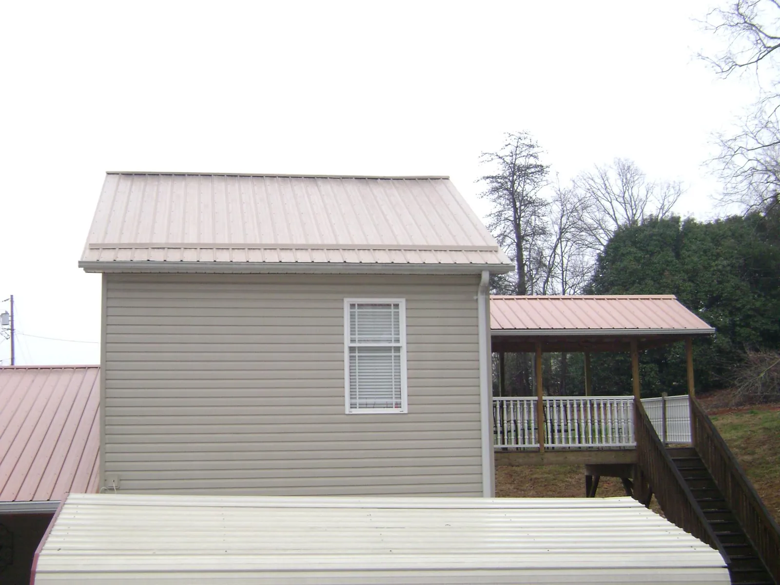 Tan metal roofs on a two story addition and attached porch, from a Roof Replacement job in Slippery Rock
